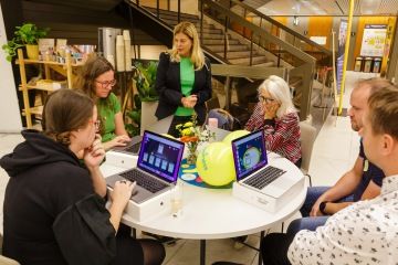 skupinba-lidi-kolem-stolu-s-pocitacemi-na-stole